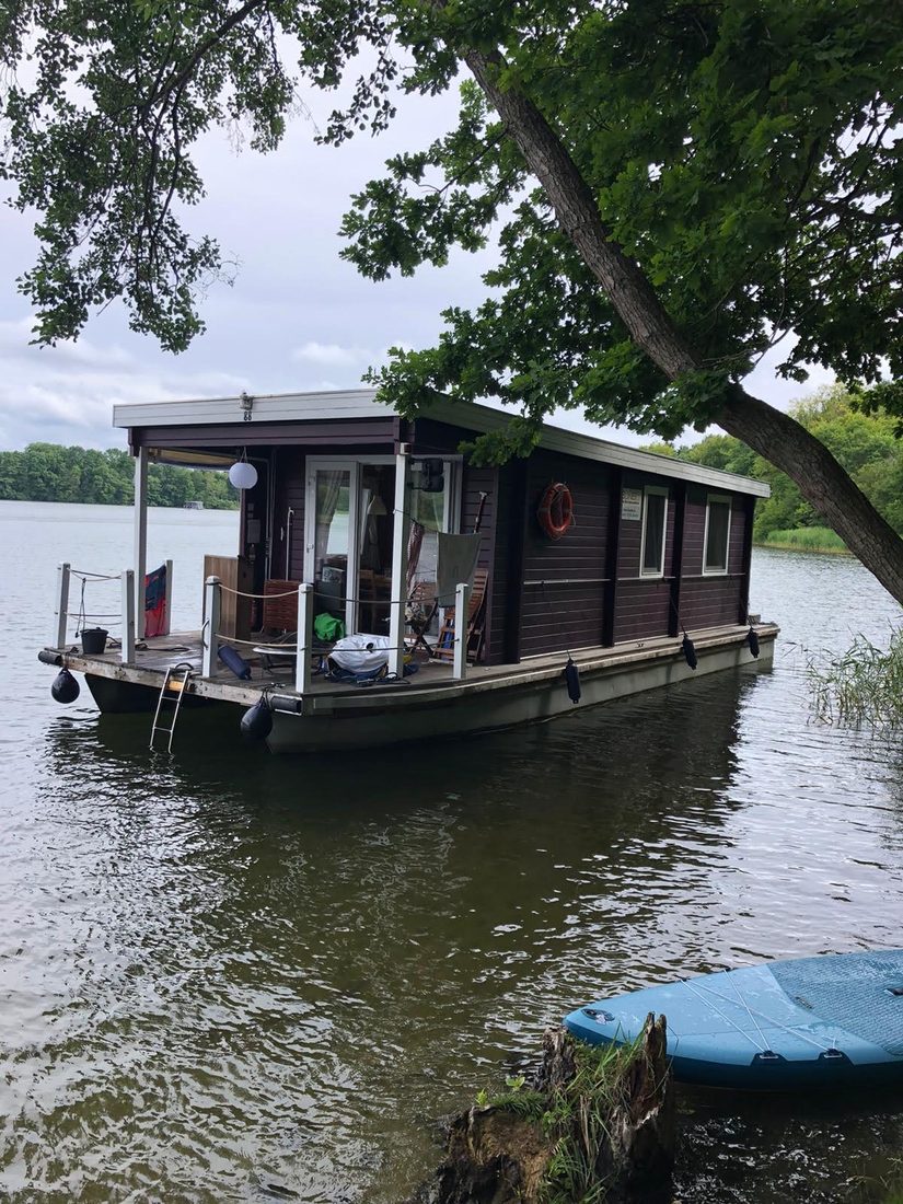 Gemietetes Hausboot-Floß mit Holzaufbau, vertäut am bewaldeten Ufer eines Sees